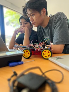 Two Hope School students testing their autonomous vehicle beside a laptop during the robotics course.